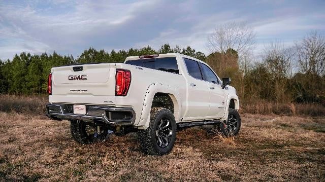Back angle of a white GMC truck next to a forest