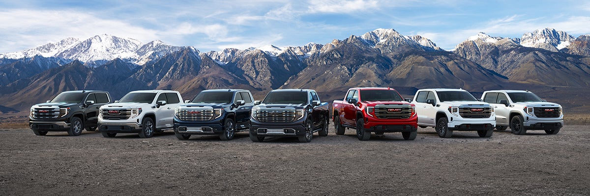 A group of GMC trucks gathered together in front of a tall mountain